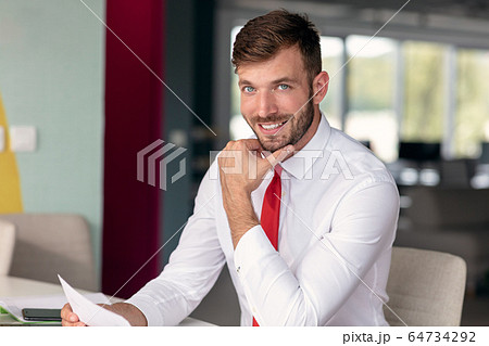 Portrait of young man sitting at his desk in the office 64734292