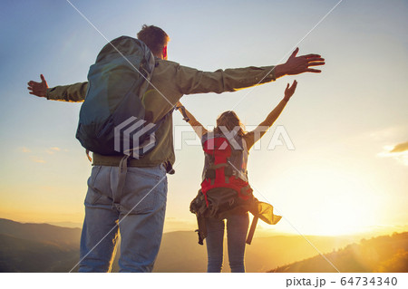 Couple with raised arms holding hands and looking at sunset 64734340