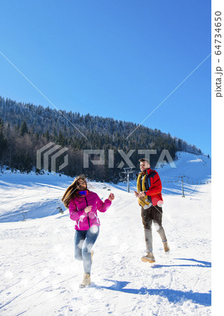 Snowball fight. Winter couple having fun playing in snow outdoors. Young joyful happy multi-racial couple. Snowball fight. Winter couple having fun playing in snow outdoors. Young joyful happy multi-racial couple. 64734650