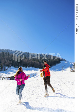 Snowball fight. Winter couple having fun playing in snow outdoors. Young joyful happy multi-racial couple. Snowball fight. Winter couple having fun playing in snow outdoors. Young joyful happy multi-racial couple. 64734663