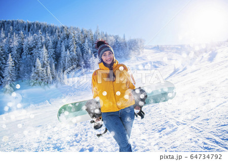 Sporty female holds snowboard in mountains in jeans 64734792