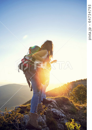 Hikers with backpacks relaxing on top of a mountain and enjoying the view of valley 64734793