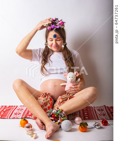 Pregnant woman smiling, touching her belly, standing over white wall. Copy space. Christmas, New year concept. 64737261