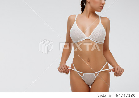 Woman in white lingerie holding laces of underwear 64747130