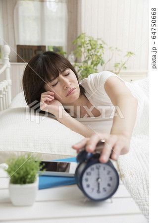 寝ぼけまなこで目覚まし時計を止める女性 寝ぼけまなこで目覚まし時計を止める女性 64750668