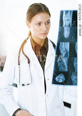 Woman-doctor examining x-ray picture in hospital. Surgeon or orthopedist at work in sunny clinic. Medicine and healthcare concept Woman-doctor examining x-ray picture in hospital. Surgeon or orthopedist at work in sunny clinic. Medicine and healthcare concept 64761915