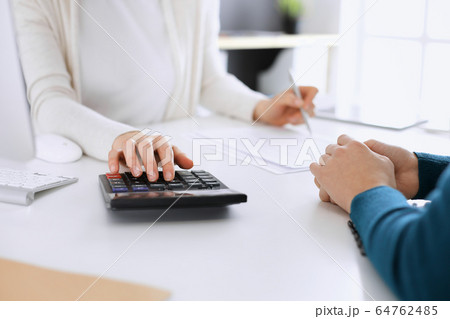 Accountant checking financial statement or counting by calculator income for tax form, hands closeup. Business woman sitting and working with colleague at the desk in office toned in blue. Tax and Accountant checking financial statement or counting by calculator income for tax form, hands closeup. Business woman sitting and working with colleague at the desk in office toned in blue. Tax and 64762485