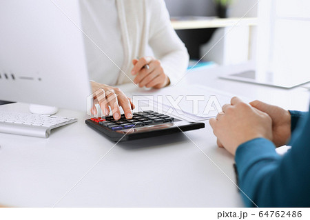 Accountant checking financial statement or counting by calculator income for tax form, hands closeup. Business woman sitting and working with colleague at the desk in office toned in blue. Tax and Accountant checking financial statement or counting by calculator income for tax form, hands closeup. Business woman sitting and working with colleague at the desk in office toned in blue. Tax and 64762486
