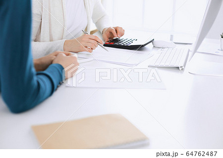 Accountant checking financial statement or counting by calculator income for tax form, hands closeup. Business woman sitting and working with colleague at the desk in office toned in blue. Tax and Accountant checking financial statement or counting by calculator income for tax form, hands closeup. Business woman sitting and working with colleague at the desk in office toned in blue. Tax and 64762487
