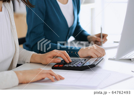 Accountant checking financial statement or counting by calculator income for tax form, hands closeup. Business woman sitting and working with colleague at the desk in office toned in blue. Tax and 64762493