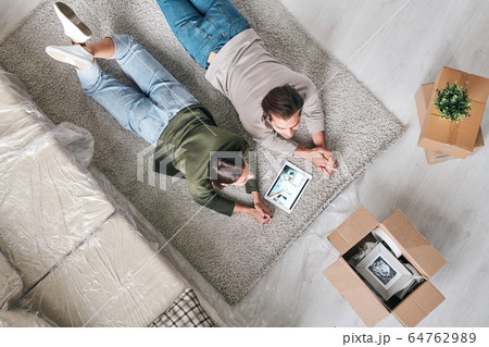 Overview of young contemporary couple in casualwear lying on unrolled rug 64762989