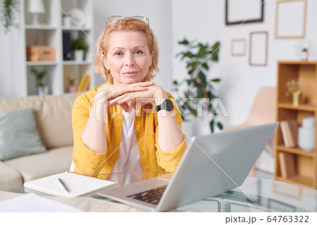 Pretty blond businesswoman in yellow shirt looking at you while working remotely Pretty blond businesswoman in yellow shirt looking at you while working remotely 64763322