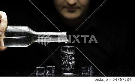 Barman pour frozen vodka from a bottle into a glass with ice. Black background Barman pour frozen vodka from a bottle into a glass with ice. Black background 64767234