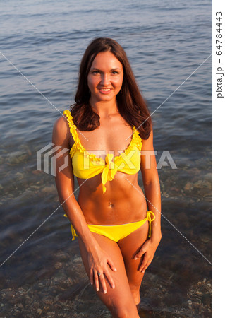 Beautiful woman with long hair in yellow swimsuit sunbathes on a sea beach Beautiful woman with long hair in yellow swimsuit sunbathes on a sea beach 64784443