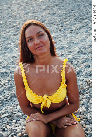 Beautiful woman with long hair in yellow swimsuit sunbathes on a sea beach 64784444