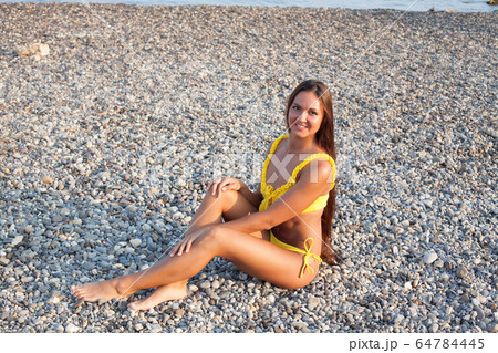 Beautiful woman with long hair in yellow swimsuit sunbathes on a sea beach 64784445