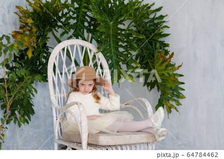 beautiful fashionable girl in a hat with fields sitting in a white chair 64784462