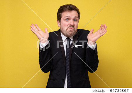 Young funny businessman in suit being uncertain Young funny businessman in suit being uncertain 64786367
