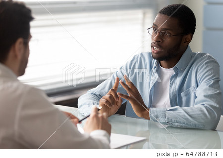 Serious african american candidate talking with businessman at job interview. Serious african american candidate talking with businessman at job interview. 64788713