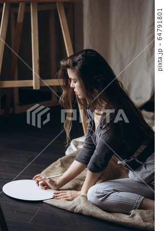 Brunette girl sitting on the floor draws with a brush 64791801