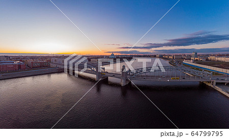 St. Petersburg Russia. Aerial panoramic view from drone to Peter the Great bridge of white nights. Bolsheokhtinsky bridge across the river Neva with evening lighting city with driving cars on highway. St. Petersburg Russia. Aerial panoramic view from drone to Peter the Great bridge of white nights. Bolsheokhtinsky bridge across the river Neva with evening lighting city with driving cars on highway. 64799795
