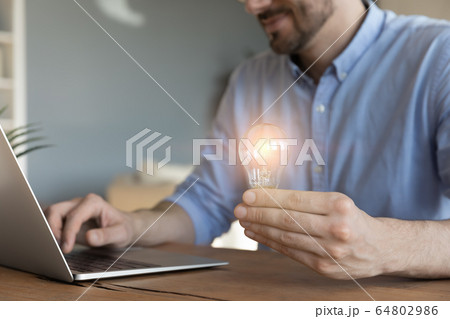 Close up businessman holding light bulb, sitting at work desk 64802986