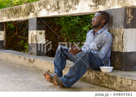 Young homeless African man with plastic bowl looking hungry 64804361