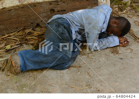 Young homeless African man lying down in the streets Young homeless African man lying down in the streets 64804424