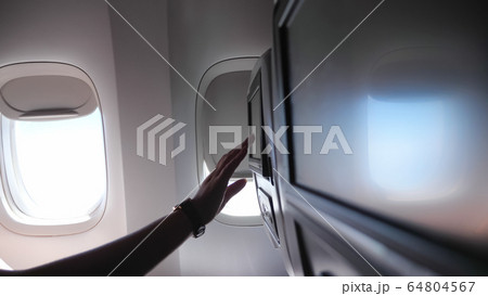 woman hand touches seatback screen in airplane closeup 64804567