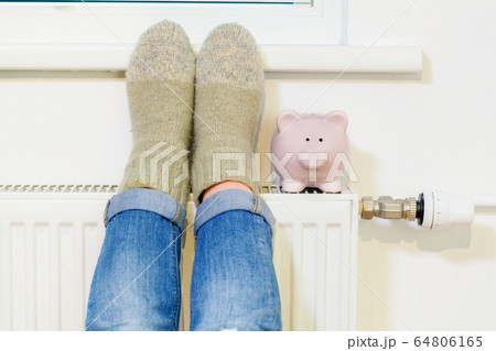 Woman warming up her feet near Piggy Bank On Radiator 64806165
