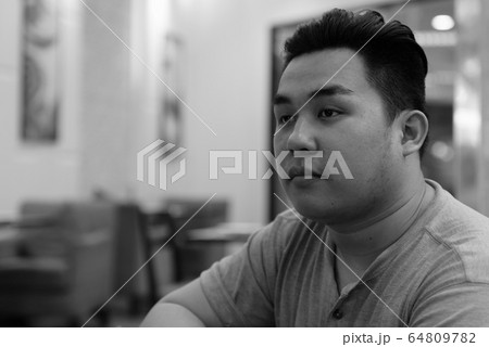 Face of young overweight Asian man thinking at the coffee shop Face of young overweight Asian man thinking at the coffee shop 64809782