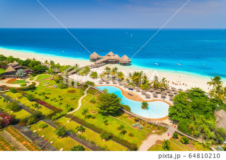 Aerial view of beautiful hotel on the sea, pool, umbrellas and green palm trees on the sandy beach Aerial view of beautiful hotel on the sea, pool, umbrellas and green palm trees on the sandy beach 64810210