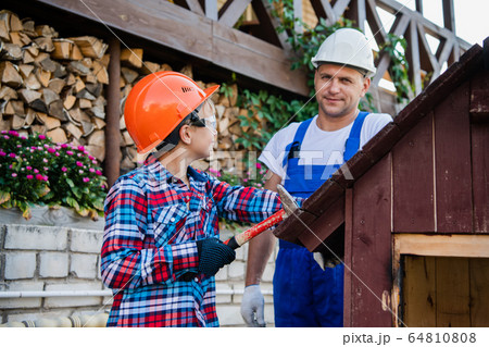Young teenager boy learns to hammer nails with his father. outdoors in the village. 64810808