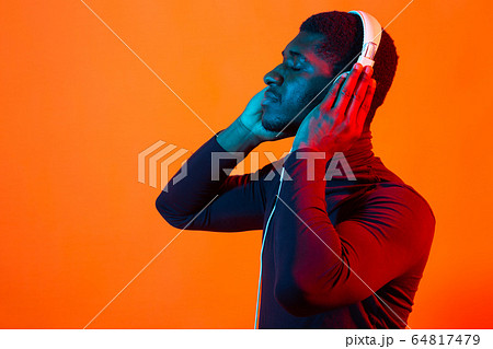 Young african-american man's listening to music in headphones in neon light with copy space. Male portrait. Concept of human emotions, facial expression, holidays or weekend, hobby, 64817479
