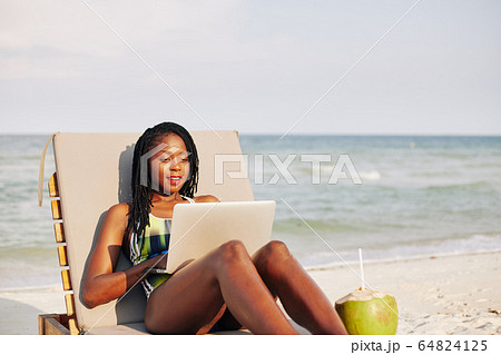 Woman resting on chaise-lounge with laptop 64824125