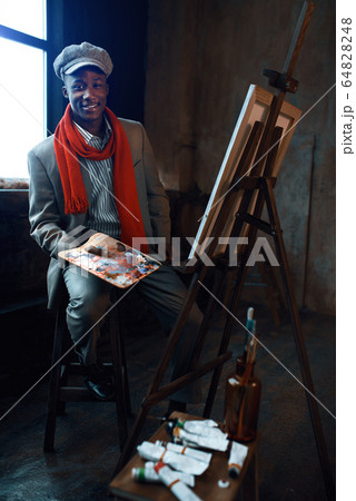 Fashionable painter with palette poses at easel Fashionable painter with palette poses at easel 64828248