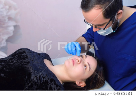 Doctor man surgeon checking up patient's moles on face before laser removal. Doctor man surgeon checking up patient's moles on face before laser removal. 64835531