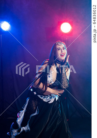 Young woman belly dancer in exotic dress with gold, dancing tribal fusion dance in studio. Young woman belly dancer in exotic dress with gold, dancing tribal fusion dance in studio. 64836012