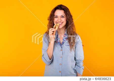 Joyful woman wears fashion pajama going to eat small delicious croissant on yellow background with copy space. Morning, breakfast and home wear concept. 64836623