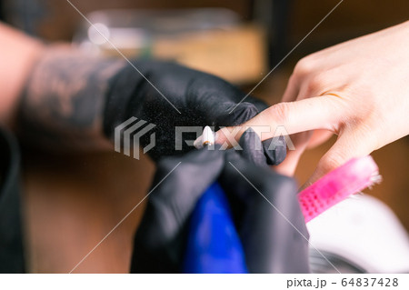 Close-up of manicurist woman removes gel shellac polish from client's nails using manicure machine. Manicure master is working with electric nail drill in beauty salon. Hardware manicure process. Close-up of manicurist woman removes gel shellac polish from client's nails using manicure machine. Manicure master is working with electric nail drill in beauty salon. Hardware manicure process. 64837428