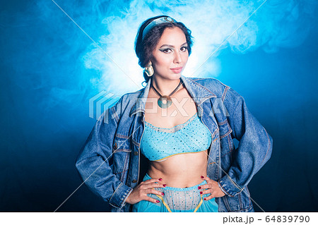 Magic, cosplay, carnival and fairy tale concept - Portrait of a young woman in the image of an Eastern fairy Princess on blue background. Magic, cosplay, carnival and fairy tale concept - Portrait of a young woman in the image of an Eastern fairy Princess on blue background. 64839790