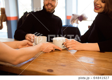 Friendly bartender serving espresso coffee to customers in the interior of a modern coffee shop. 64841927