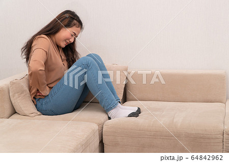 Unhappy Asian woman sitting on sofa and holding on 64842962