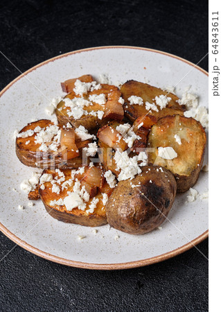 Slices of baked potatoes with feta cheese and bacon on a white plate on a dark concrete background Slices of baked potatoes with feta cheese and bacon on a white plate on a dark concrete background 64843611