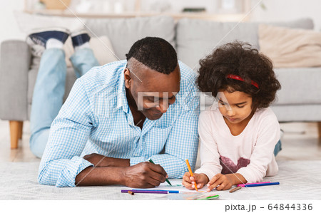 Quiet family times. Pretty African American girl drawing on floor with her granddad 64844336