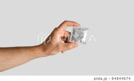 Safe sex concept. Young guy holding condom in wrapper on light grey background, empty space. Panorama Safe sex concept. Young guy holding condom in wrapper on light grey background, empty space. Panorama 64844674