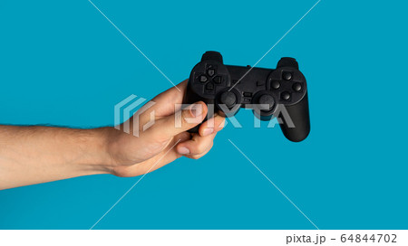 Stay home hobby. Millennial guy holding video game controller on blue background, closeup. Panorama Stay home hobby. Millennial guy holding video game controller on blue background, closeup. Panorama 64844702