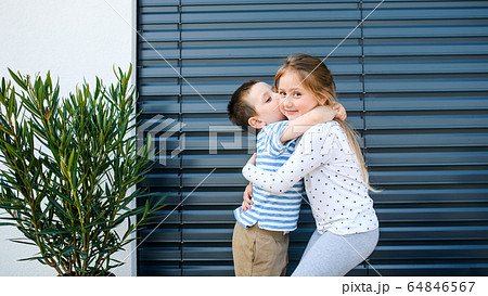 Small girl and boy standing outdoors at home, hugging. Small girl and boy standing outdoors at home, hugging. 64846567
