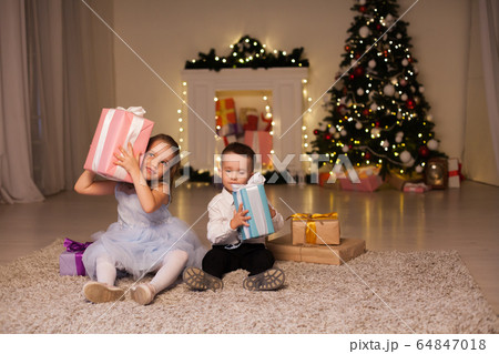 Kids open gifts at Christmas tree holiday New Year's Eve lights garlands 64847018