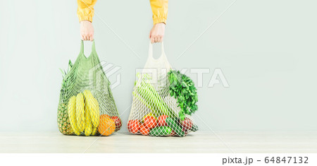 hands hold two mesh shopper bags with fruit and 64847132